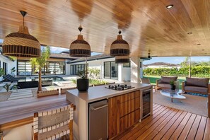 A modern outdoor kitchen area with a built-in stove, wooden flooring, and hanging wicker pendant lights.