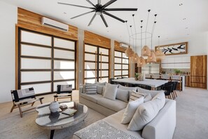 A modern living room with a sofa, coffee table, and chairs, a dining area with a table and chairs, and a kitchen area with cabinets and a countertop.