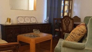 A living room with a wooden coffee table, a green armchair, a wooden cabinet, and a mirror on the wall. - Super Comfy Room at a Great Location  (Detroit)