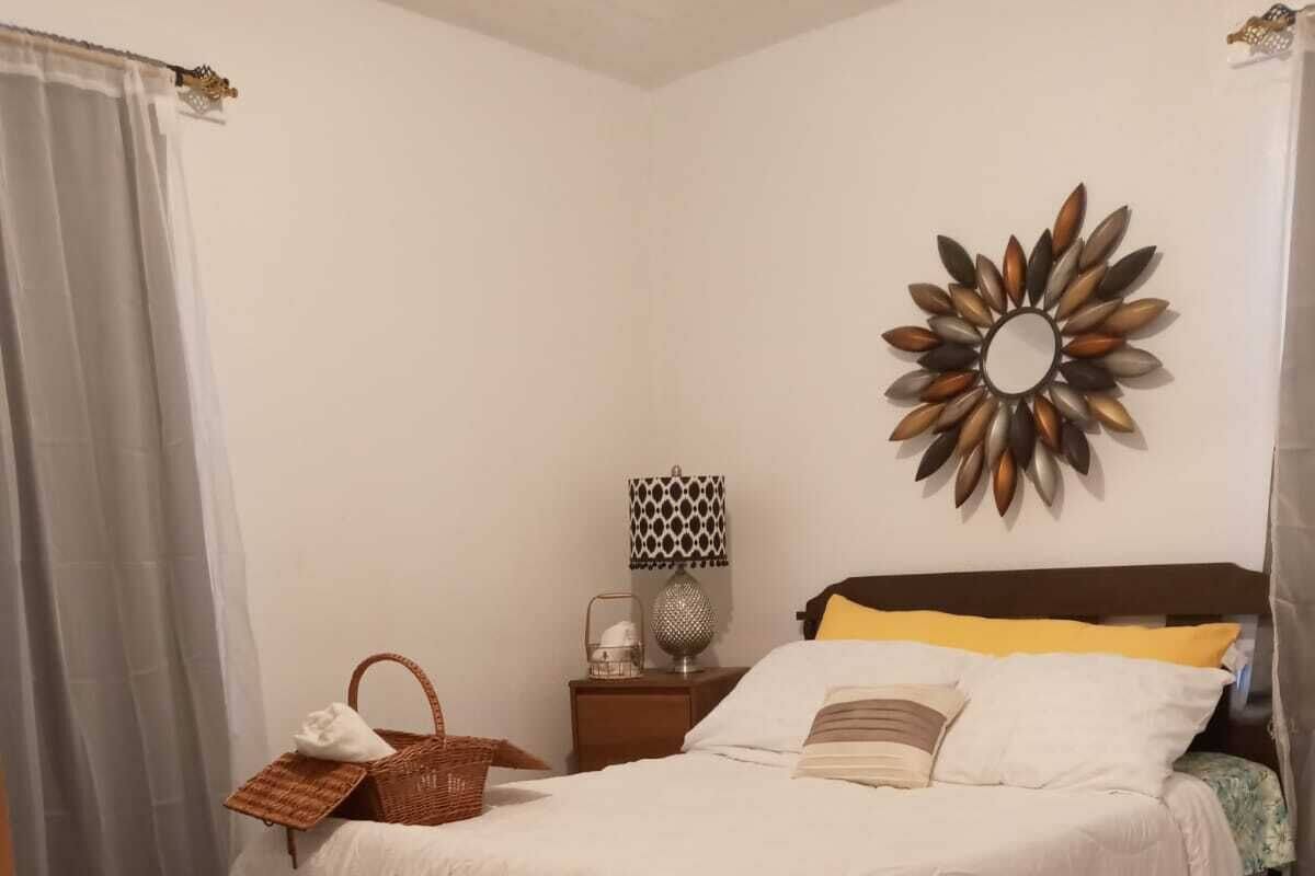 A neatly arranged bedroom with a bed, a bedside table, a lamp, and a decorative wall piece.