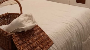 A neatly made bed with white linens, a wicker basket with a white towel, and a wooden headboard. - Super Comfy Room at a Great Location  (Detroit)