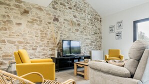 Ein Wohnzimmer mit Steinwand, Fernseher, gelben Sesseln, einer Couch und einem Korbstuhl.