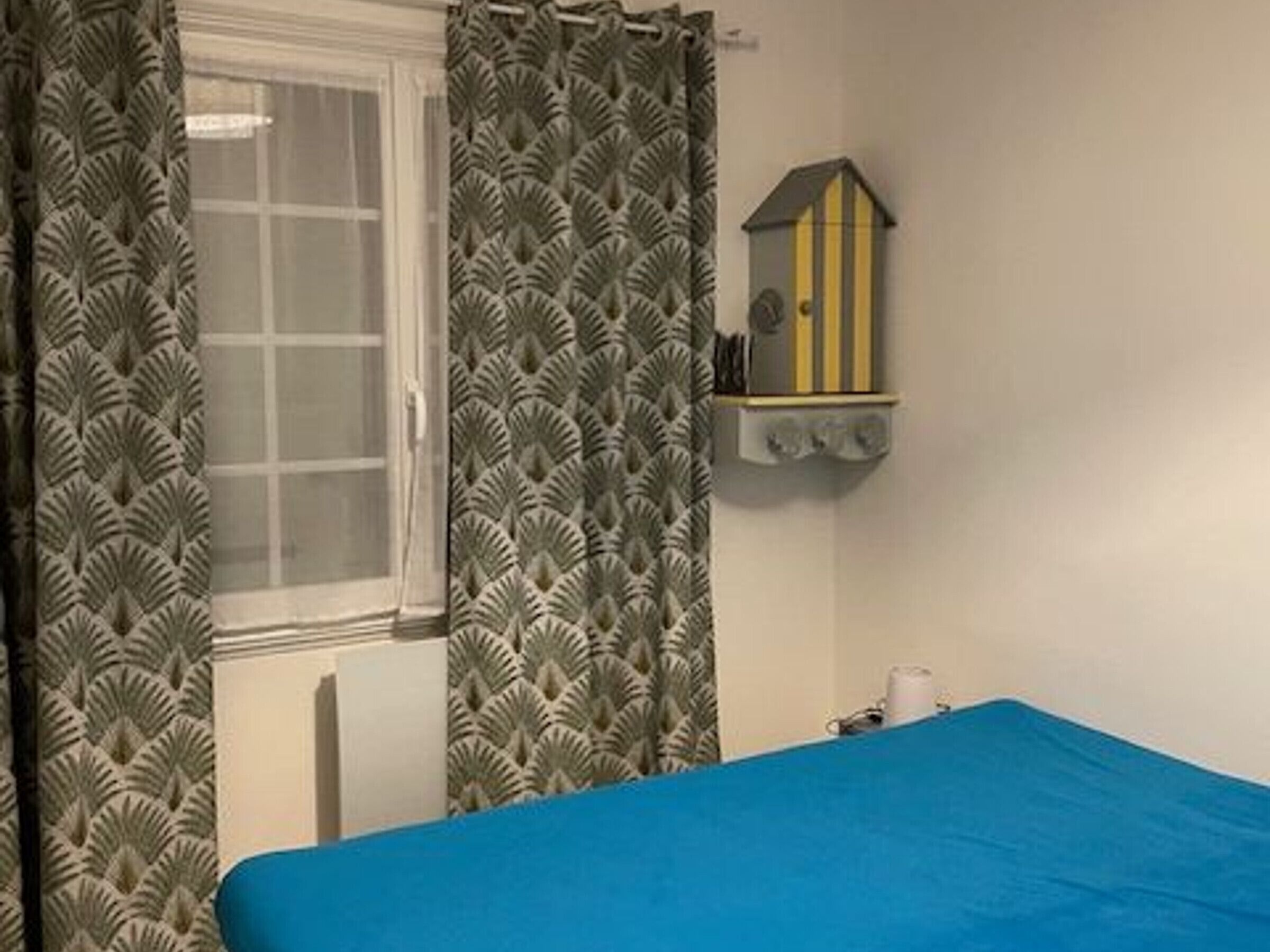 A room with a bed, a window with curtains, a wall-mounted birdhouse, and a radiator.