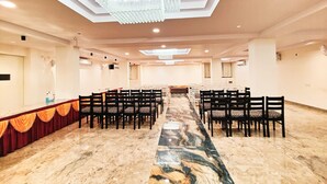 Un salón de conferencias con una larga mesa, filas de sillas, suelo de mármol y un candelabro.