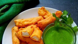 Un plato de aperitivos fritos dorados, salsa verde para mojar y guarnición de hierbas frescas.