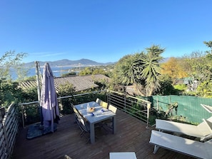 A wooden deck with a table and chairs, overlooking a scenic view of the sea and mountains.