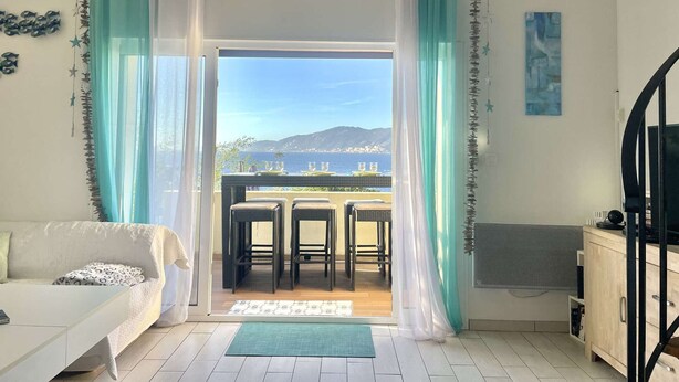 A room with a bed, a desk, a chair, a table, and a view of the sea.