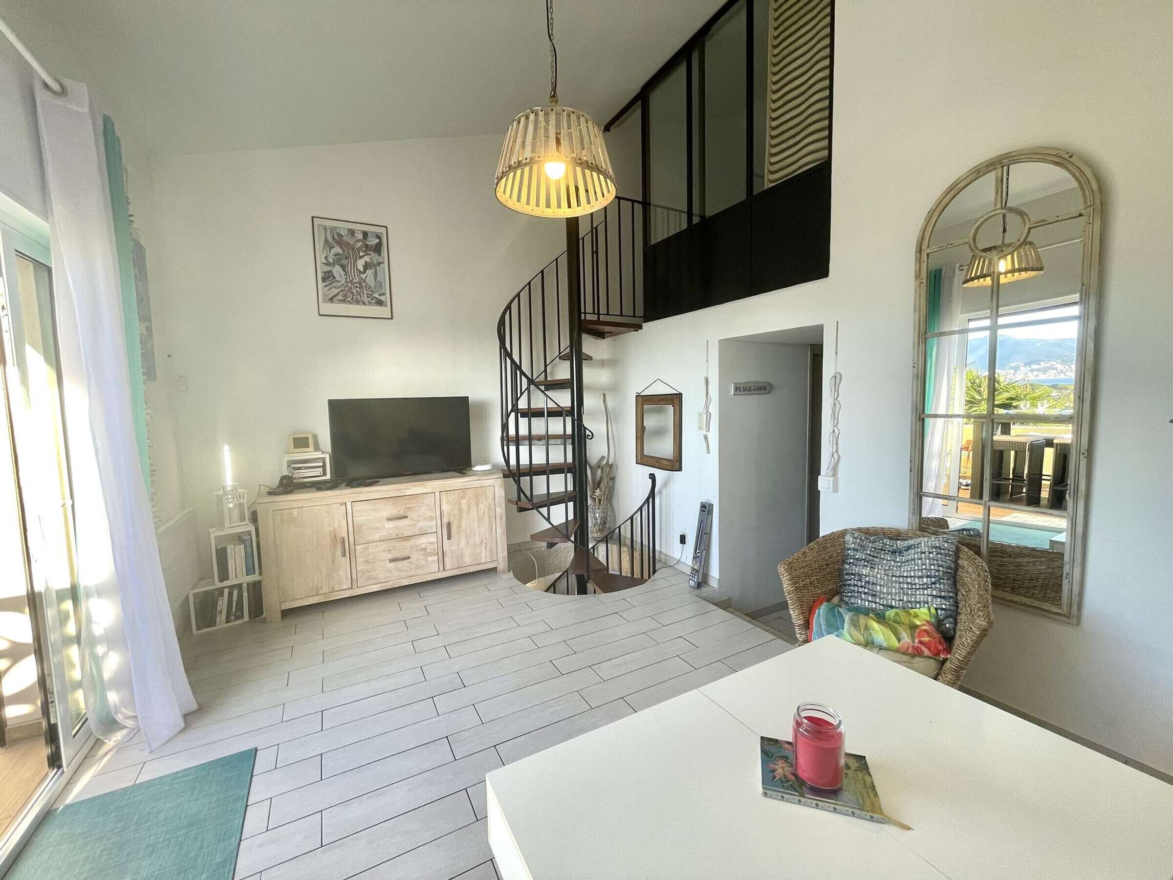 A modern living room with a staircase, a dining area, and a view of the outdoors.