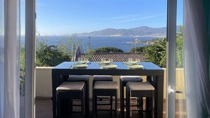 A dining area with a table set for four, overlooking a coastal view with mountains and a cityscape.
