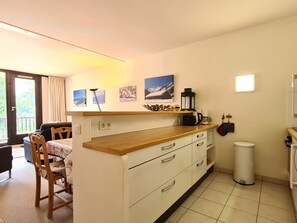 Uma cozinha compacta com bancada de madeira, armários brancos e um pequeno cesto de lixo.