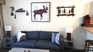 A living room with a dark grey sofa, two side tables with lamps, a coffee table, a framed moose picture, and a wooden wall decoration. - Deluxe Mountain Fox Suite Jiminy Peak - Ski On Off - Fully Redone Decor (Hancock)