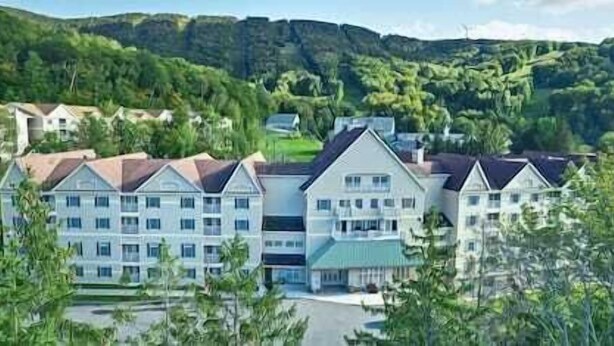 A row of multi-story buildings with a uniform architectural style, likely a hotel or resort, set against a backdrop of green hills and trees. - Deluxe Mountain Fox Suite Jiminy Peak - Ski On Off - Fully Redone Decor (Hancock)