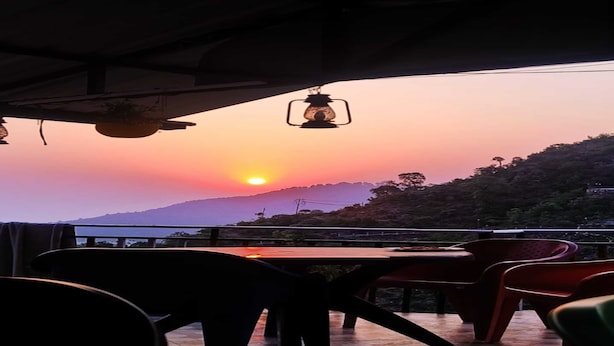 Un ristorante con tavoli all'aperto, vista su un tramonto e montagne.