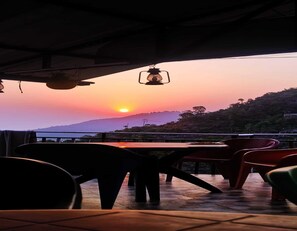A restaurant with outdoor seating overlooking a sunset and mountains. - Kasana Club Mussoorie (Dehradun)
