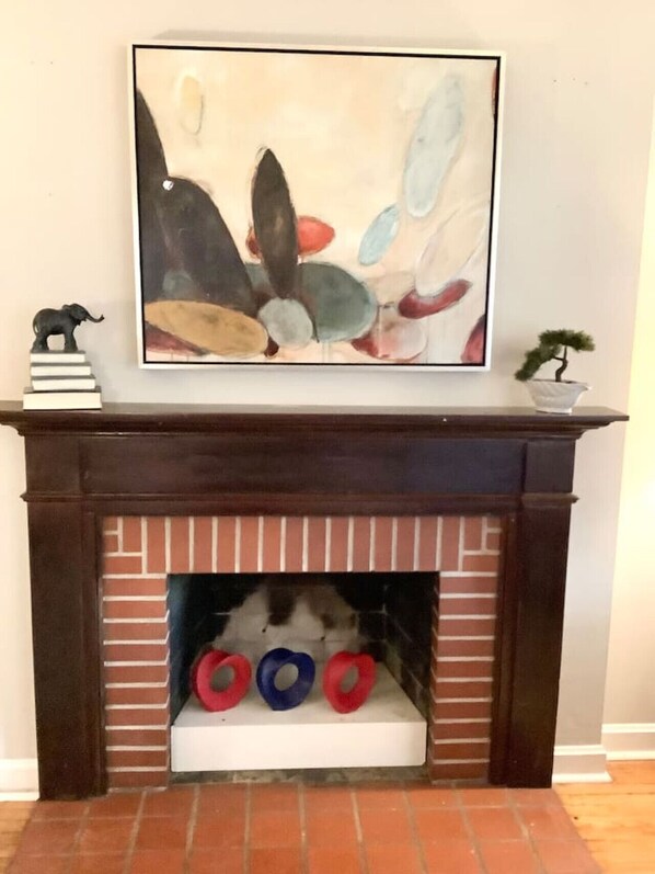 Una chimenea con un repisa que muestra un cuadro abstracto enmarcado, una pequeña figura de elefante y un bonsái.