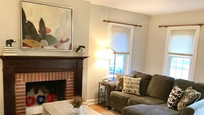 A living room with a fireplace, a sofa, a coffee table, and a painting on the wall. - The House Hotels - Superior Road (Cleveland Heights)