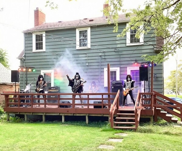 Une scène a été installée devant une maison dotée d’une terrasse en bois et d’un escalier menant à celle-ci.