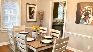 A dining room with a wooden table set for four, white chairs, and a vase with yellow flowers. - The House Hotels - Superior Road (Cleveland Heights)