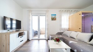 Ein modernes Wohnzimmer mit Flachbildfernseher, einer Couch, einem Couchtisch und einer Glasschiebetür, die zu einem Außenbereich führt.