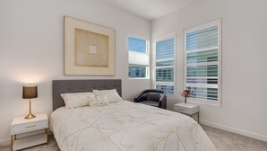 Quarto com uma cama grande, mesa de cabeceira com luminária, cadeira e janela com persianas.
