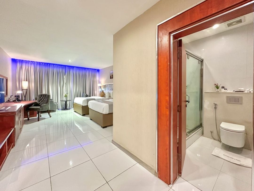 A hotel room with a bed, a desk, a chair, a bathroom with a toilet and shower, and a curtain.