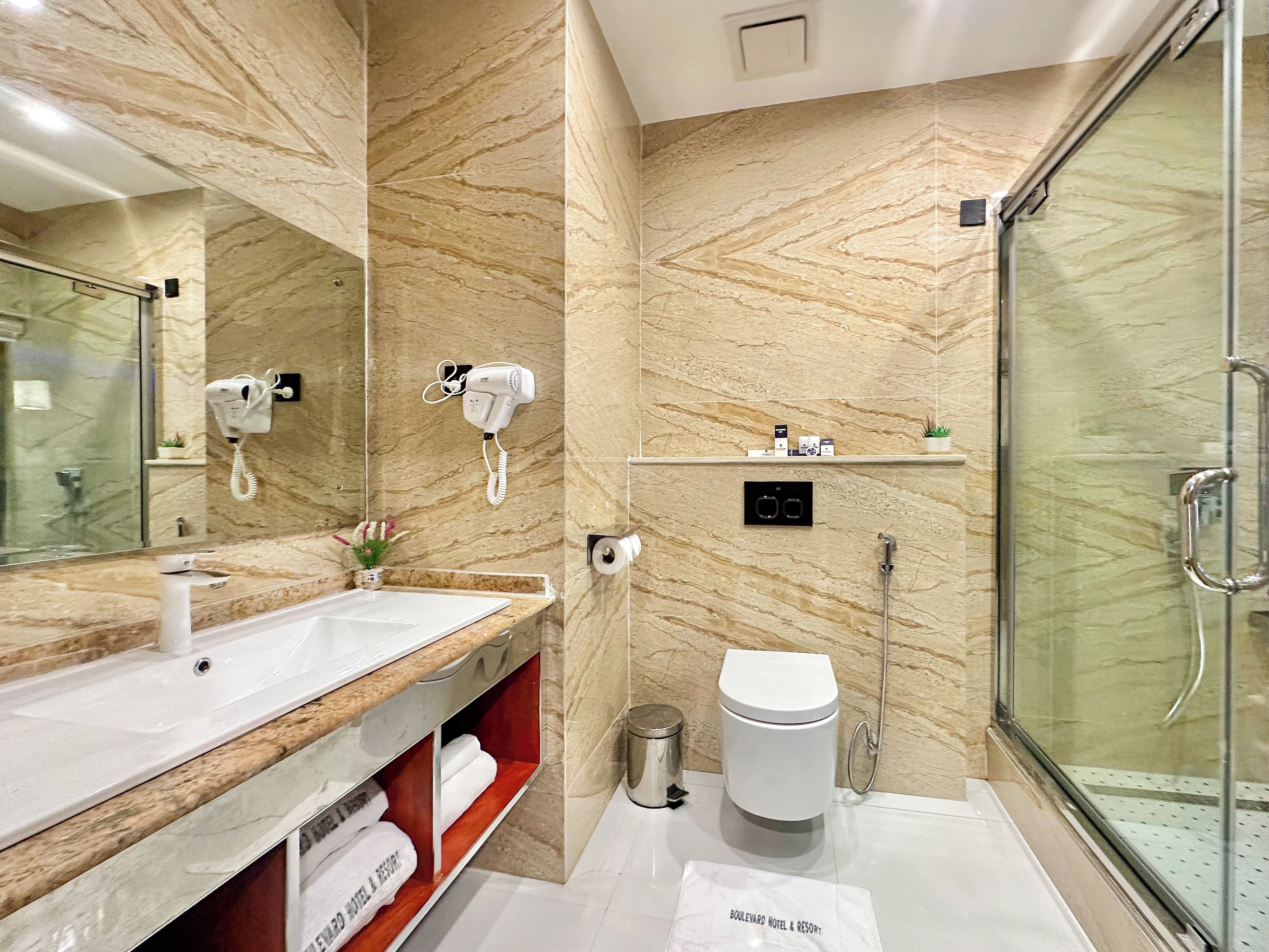 A modern bathroom with a marble wall, a glass shower enclosure, a vanity with a sink, and a towel rack.