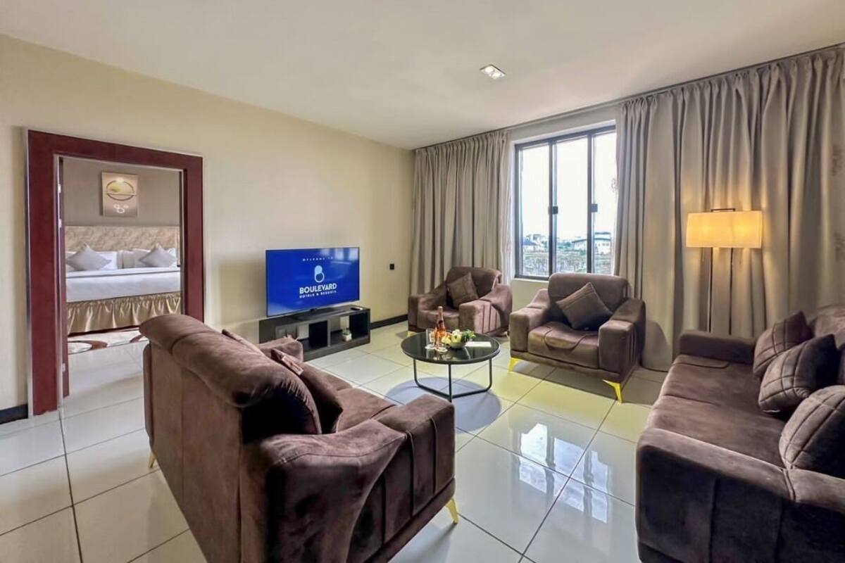 A hotel room with a bed, a television, two sofas, a coffee table, and a large window with curtains.