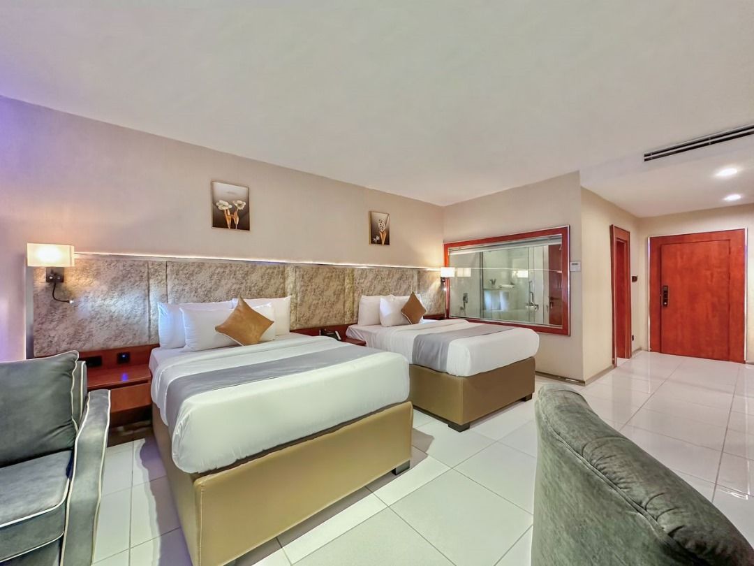 Habitació d'hotel amb dos llits, un sofà, un mirall i una porta vermella.