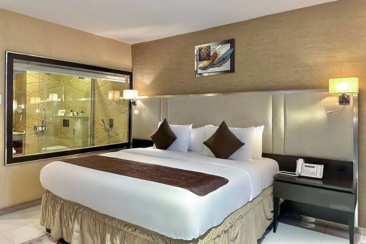 A hotel room with a large bed, a bedside table with a phone, and a glass-enclosed shower area.