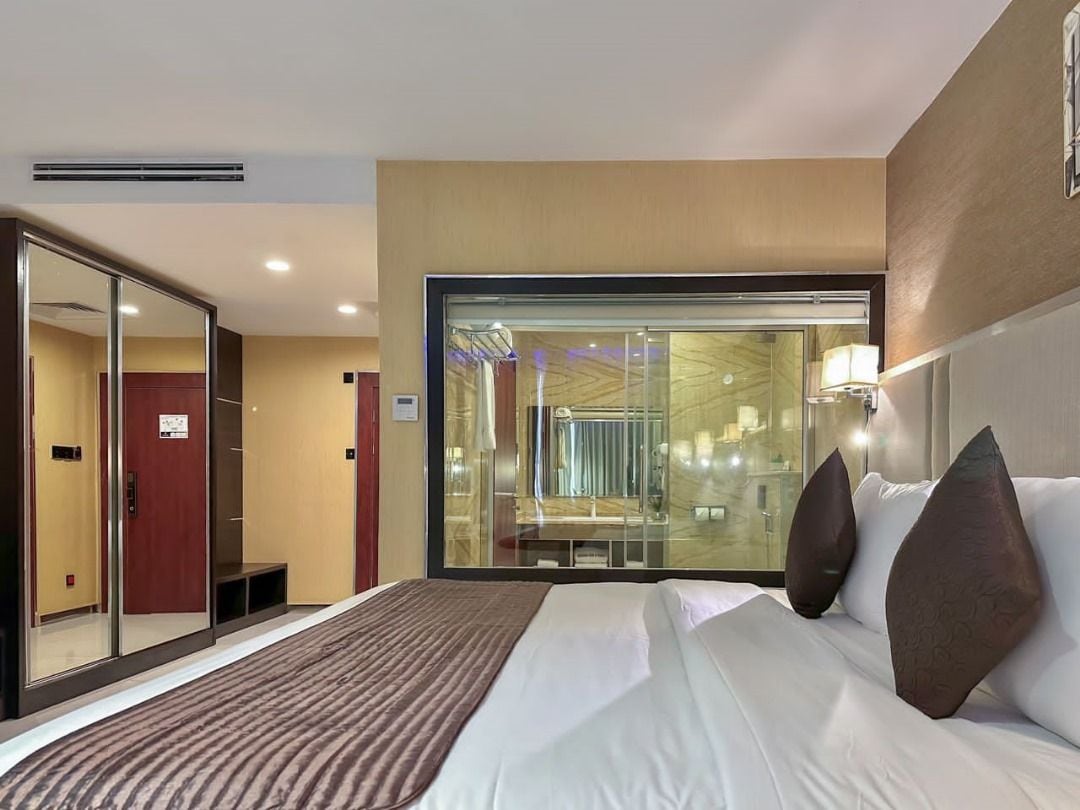 Une chambre d’hôtel avec un grand lit, une cloison en verre et une vue sur l’intérieur de l’hôtel.