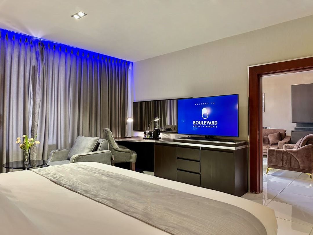 Ett modernt hotellrum med en stor säng, ett skrivbord med en platt-TV, en sittgrupp med en soffa och utsikt över omgivningarna.