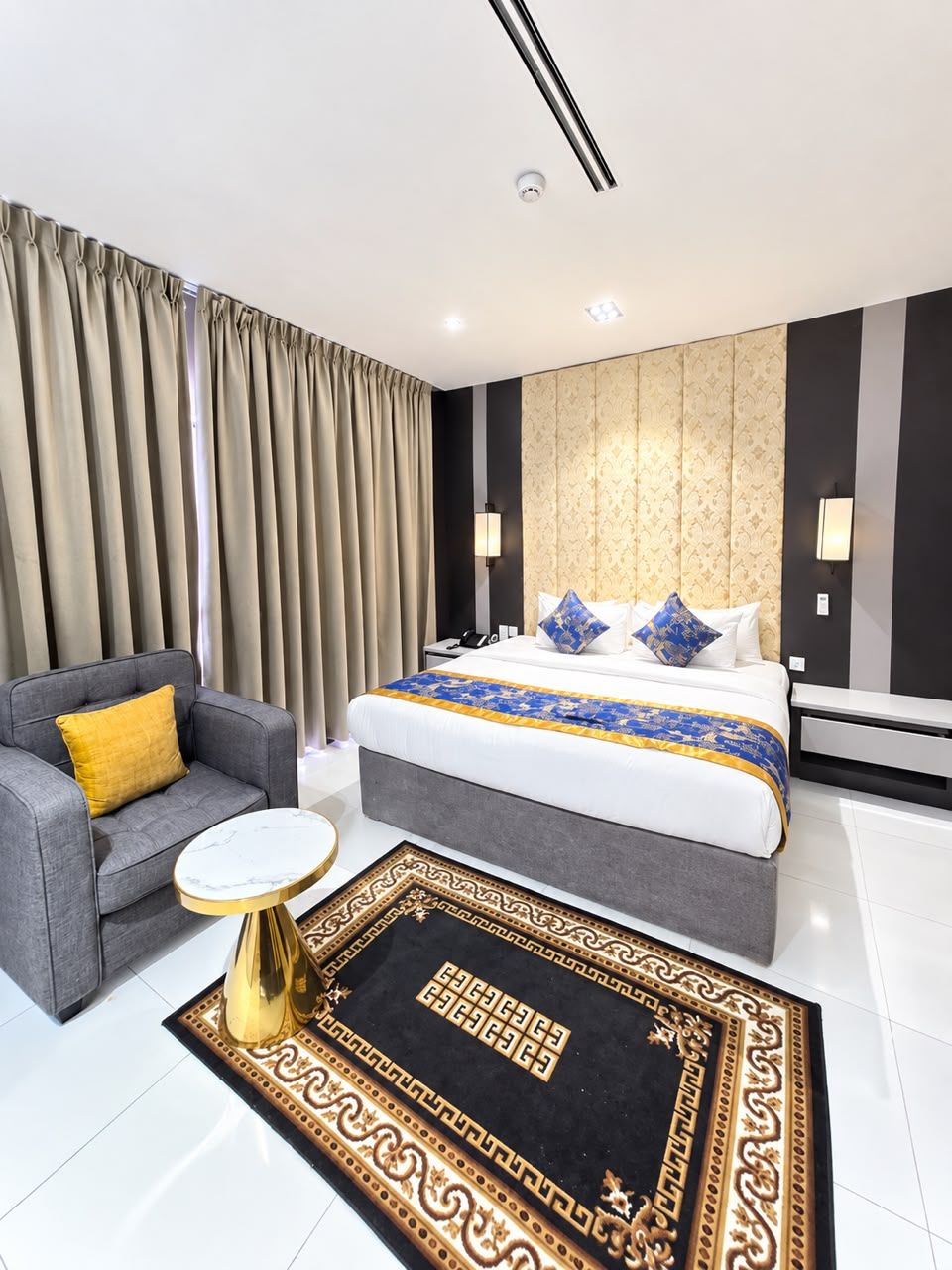 A modern hotel room with a large bed, a sofa, a small round table, and a decorative rug.