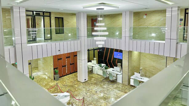 Un moderno vestíbulo de hotel con balaustrada de vidrio, un candelabro y un mostrador de recepción.