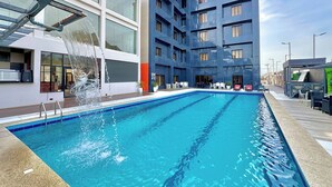Un hotel moderno con piscina, zona de estar exterior y un espacio cubierto con pared verde.