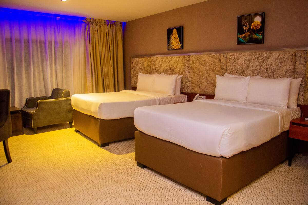 A hotel room with two beds, a desk, a chair, and a large window with curtains.