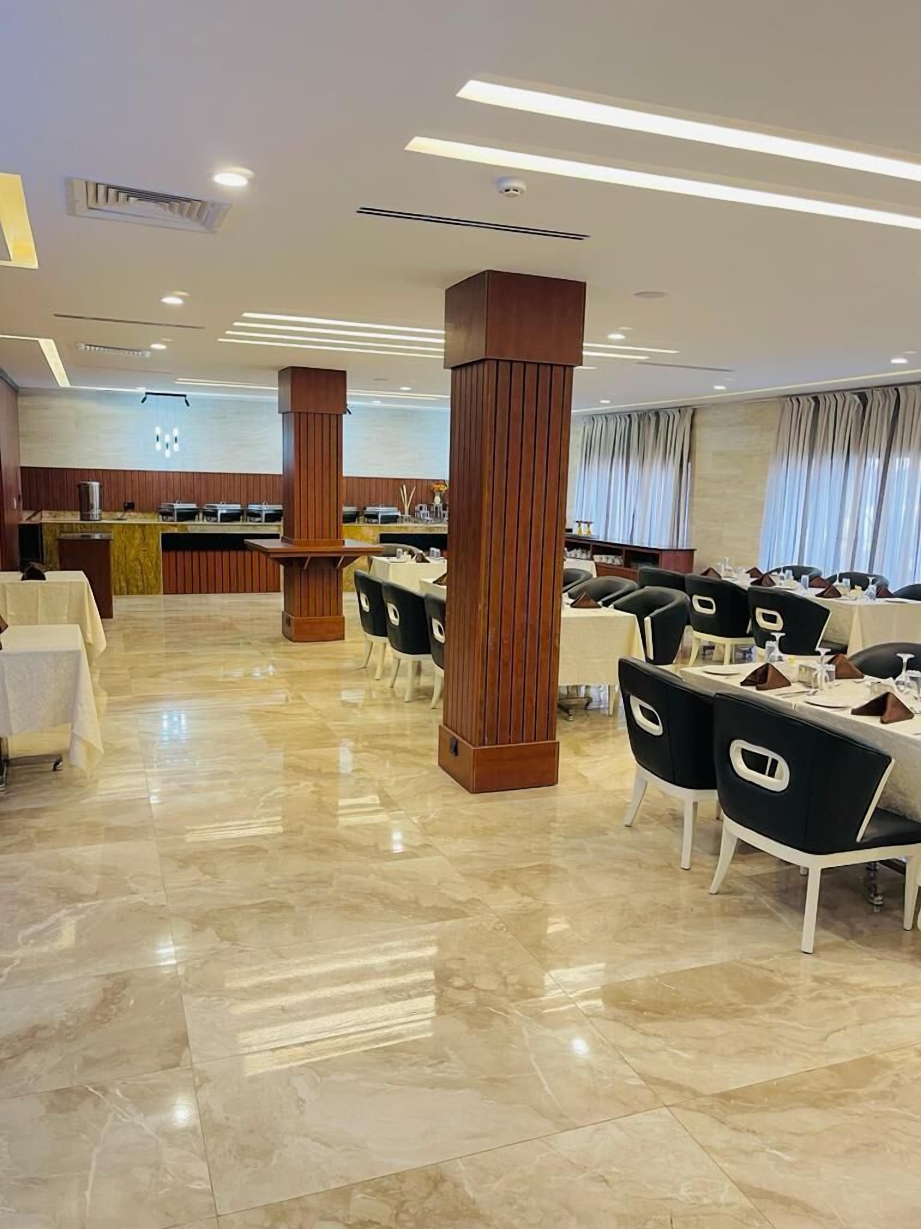 A spacious dining area with marble flooring, wooden pillars, and black and white chairs.
