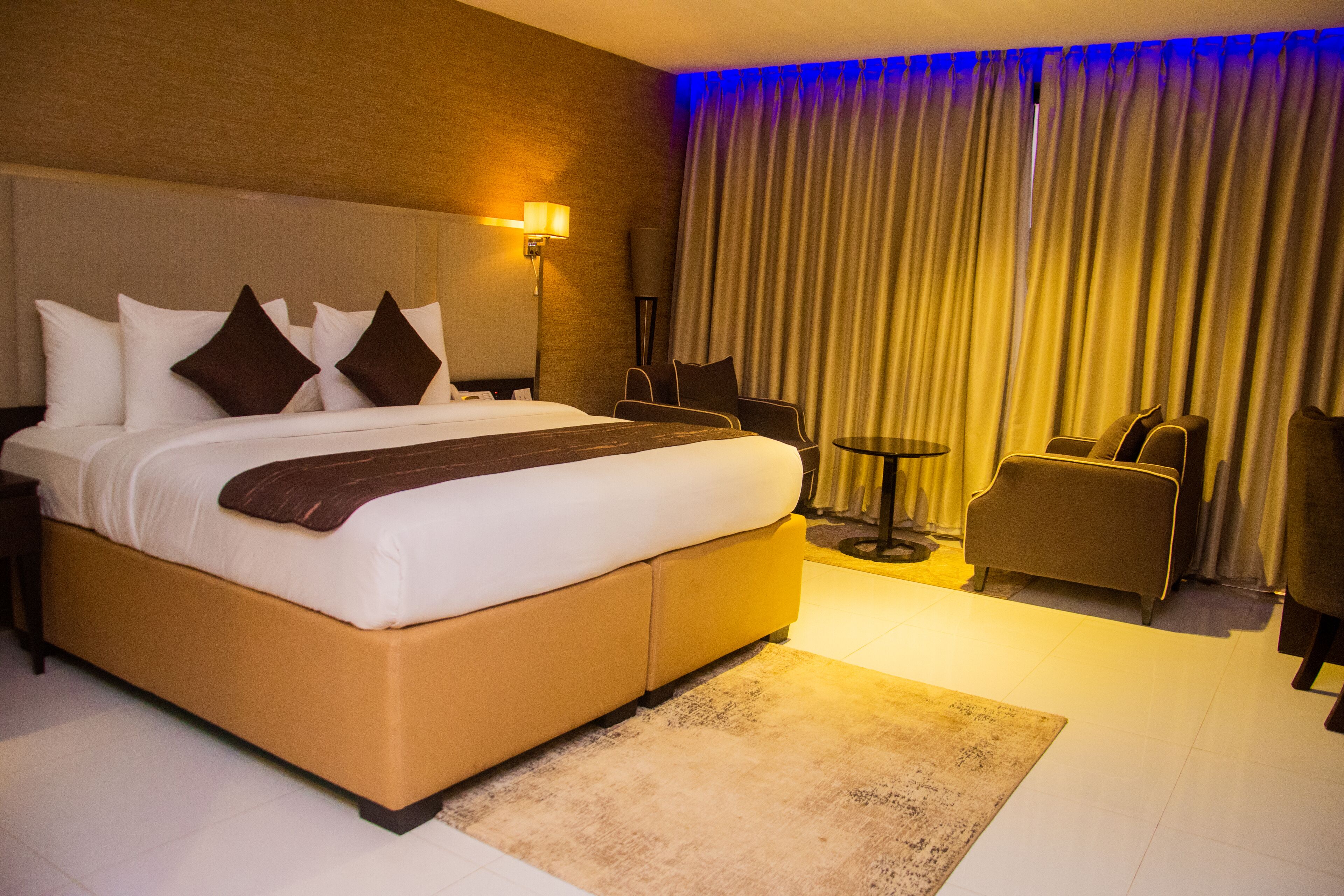A hotel room with a large bed, a desk, a chair, and a small table.