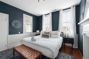 Quarto com uma cama grande, duas mesas de cabeceira, um banquinho e um relógio de parede.