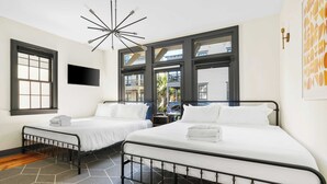 Quarto de hotel com duas camas, televisão, um candelabro moderno e janelas amplas.
