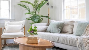 Una sala de estar acogedora con un sofá, una butaca, una mesita de centro y una planta grande.