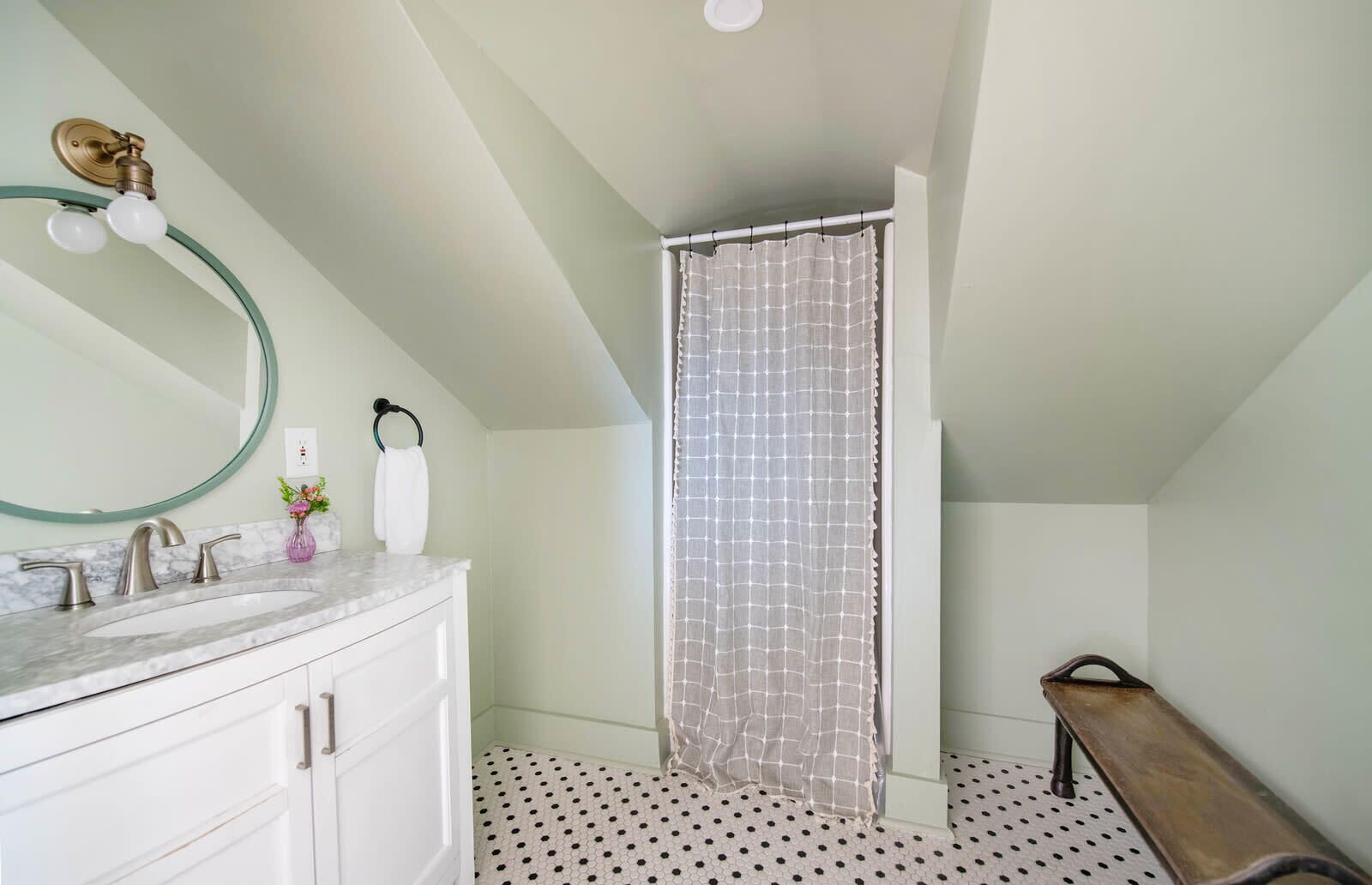 Une salle de bain avec un meuble-lavabo blanc, un miroir rond, un rideau de douche et un banc.
