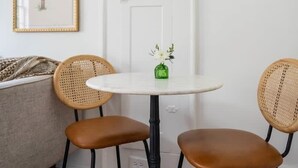 Una habitación con una puerta blanca, una mesa redonda con dos sillas, un florero verde con flores y un cuadro en la pared.