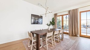 A dining area with a wooden table and chairs, a large window with curtains, and a ceiling light fixture. - Newly Built, 4bd Luxury Suite steps to King! (Charleston)