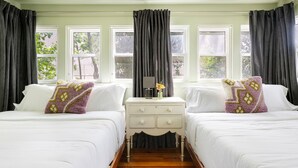 A room with two beds, a nightstand, and a window with curtains.