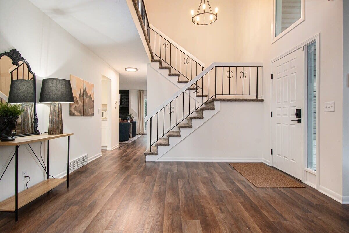 A modern interior with a wooden floor, a staircase with metal railings, and a chandelier.