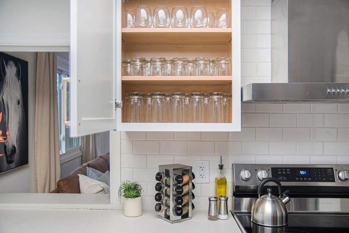 A kitchen with a white countertop, a stainless steel stove, a spice rack, and a cabinet with glassware.