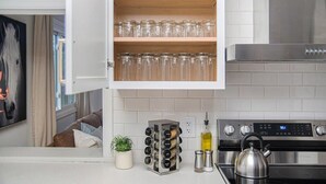 Una cocina con cubierta blanca, estufa de acero inoxidable, especiero y un armario con cristalería.