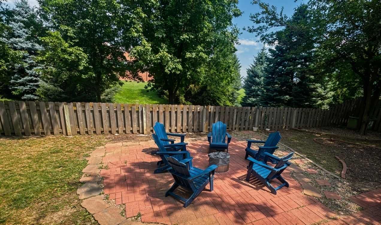 Un patio con cuatro sillas Adirondack azules y una pequeña mesa, rodeado por una valla de madera y árboles.