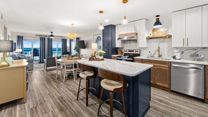 A modern kitchen with a central island, bar stools, and a dining area with a view. - 🌴 Oceanfront Pinnacle Port Escape | Sleeps 8 | Last Week of July Available! (Panama City Beach)
