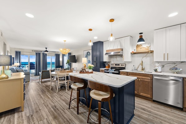 A modern kitchen with a central island, bar stools, and a dining area with a view.